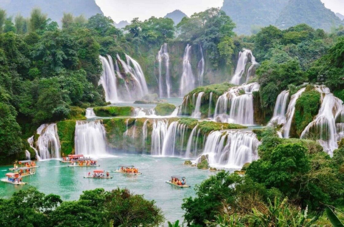 A scenic waterfall cascading through lush greenery with boats on the turquoise water.