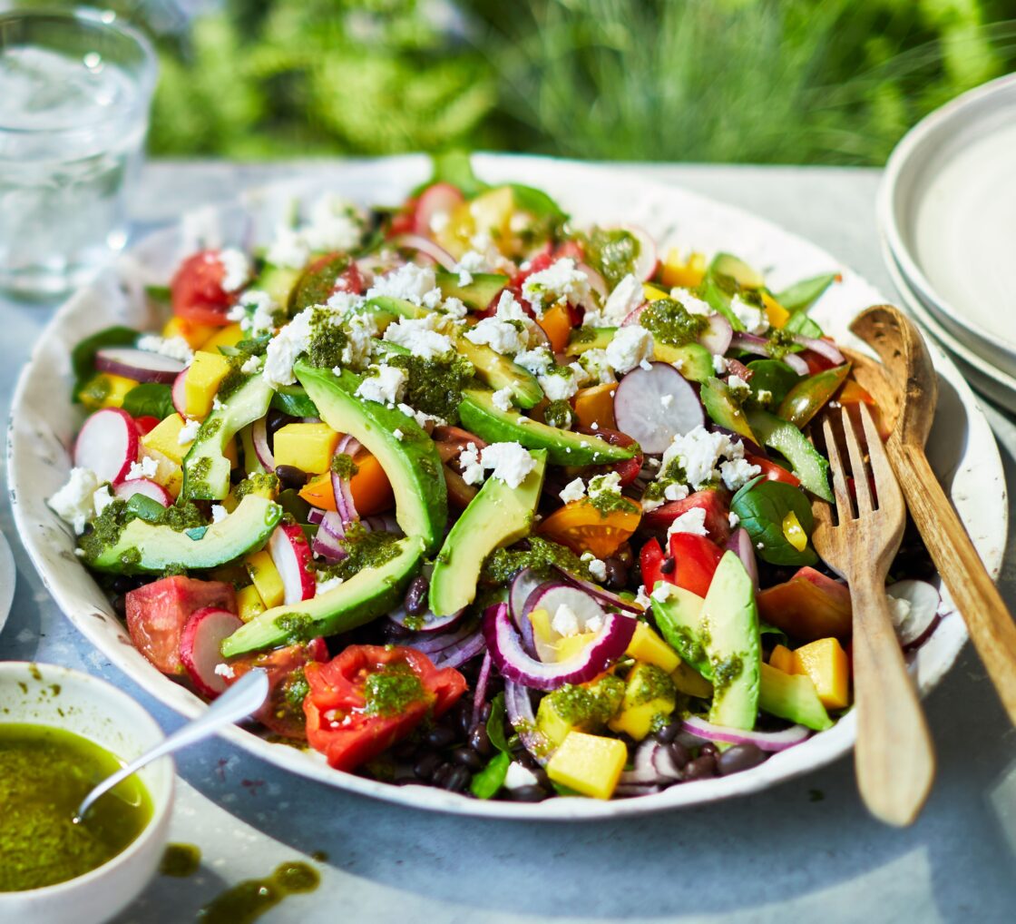 Colorful salad with avocado, radish, tomatoes, and cheese on a white plate outdoors.