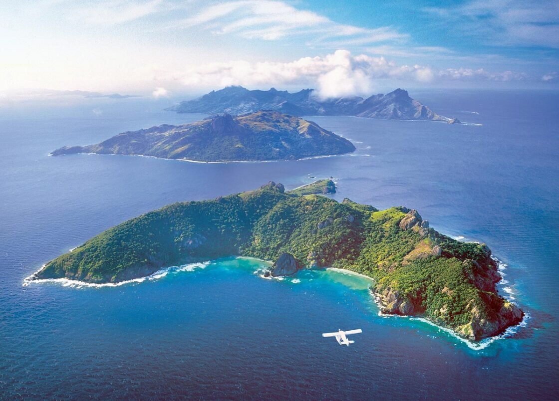 Aerial view of tropical islands with clear blue water and a seaplane flying nearby.