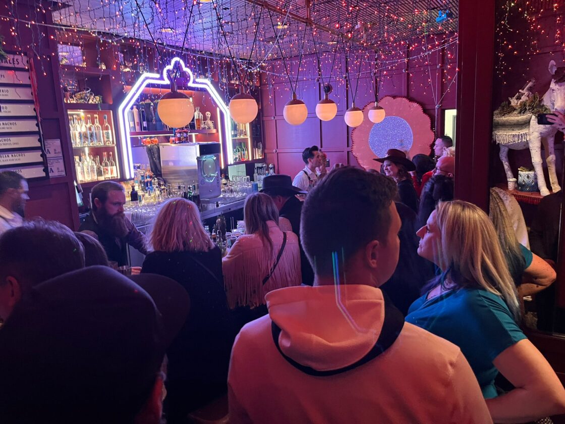 A crowded bar with neon lights and people socializing.