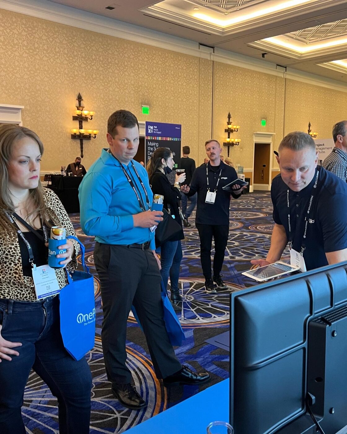 People at a conference booth, engaging with a presentation screen.