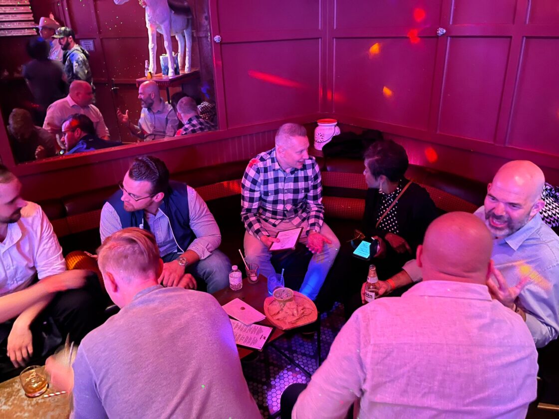 People sitting and talking in a dimly lit bar with drinks on the table.