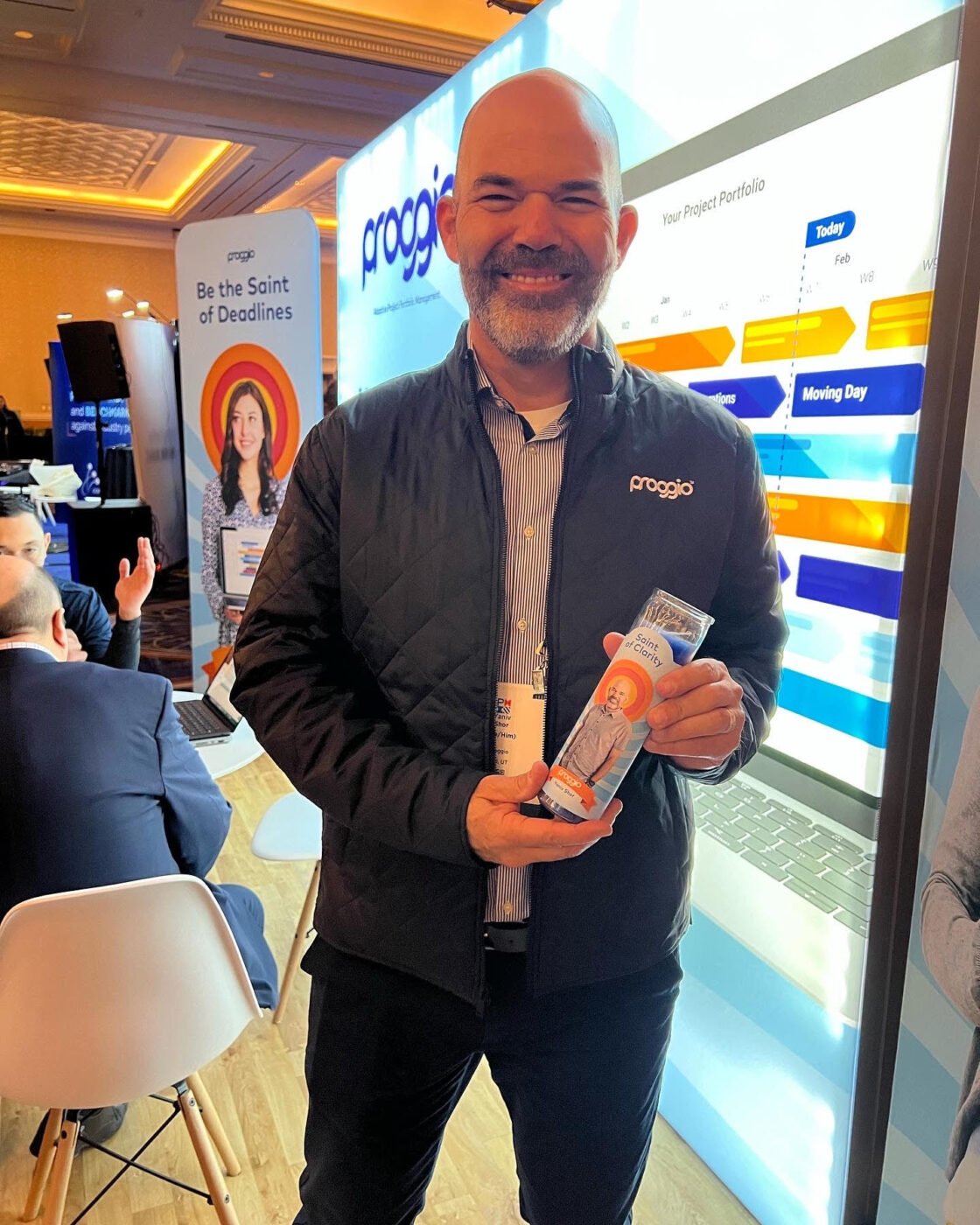 Smiling man at a conference booth holding a brochure, surrounded by bright displays.