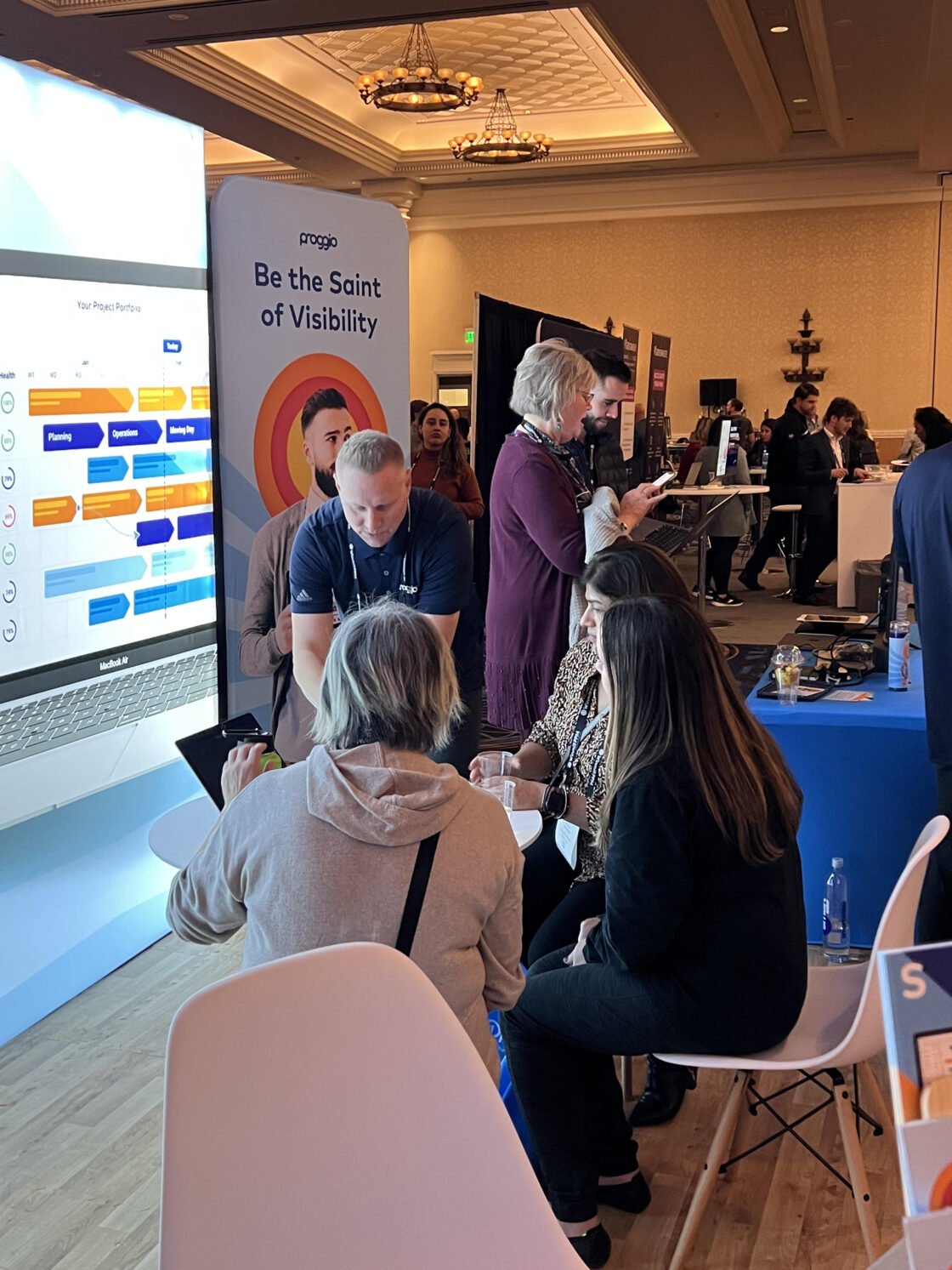 People interacting at a tech booth in a conference setting.