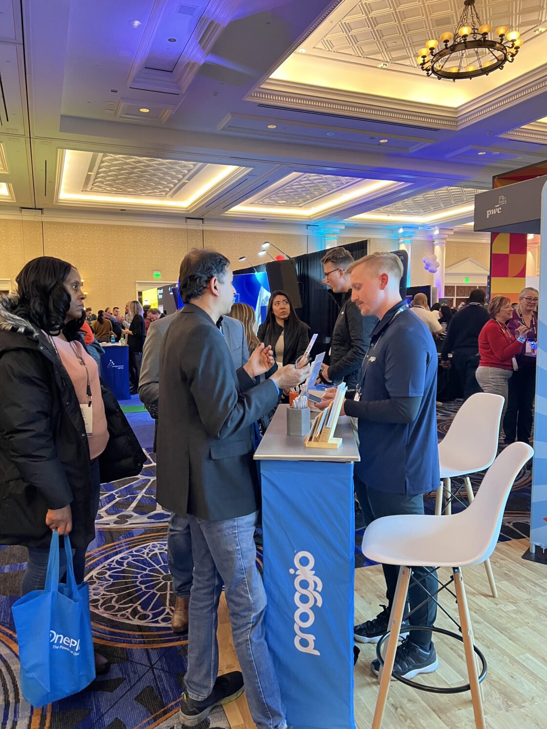 People interacting at a busy conference booth with brochures and displays.