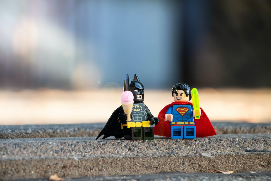 Lego Batman and Superman sitting on steps, sharing ice cream.