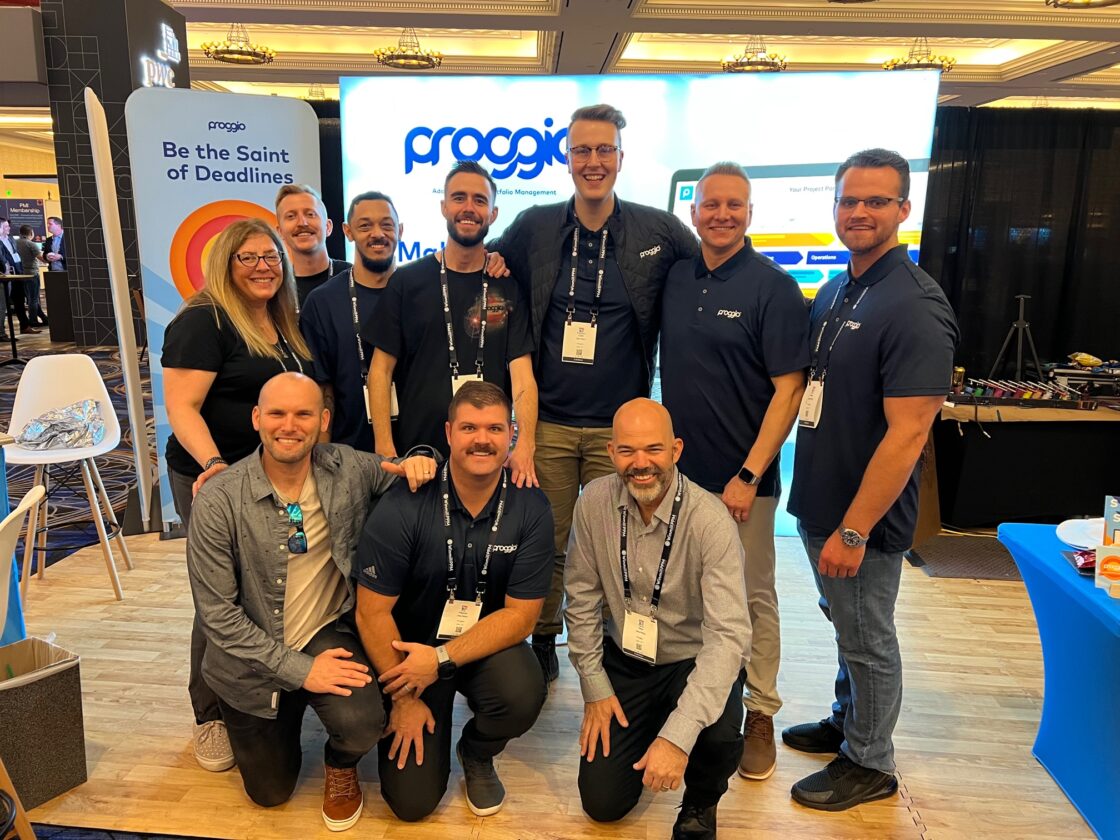 A group of people smiling and posing together at a conference booth.