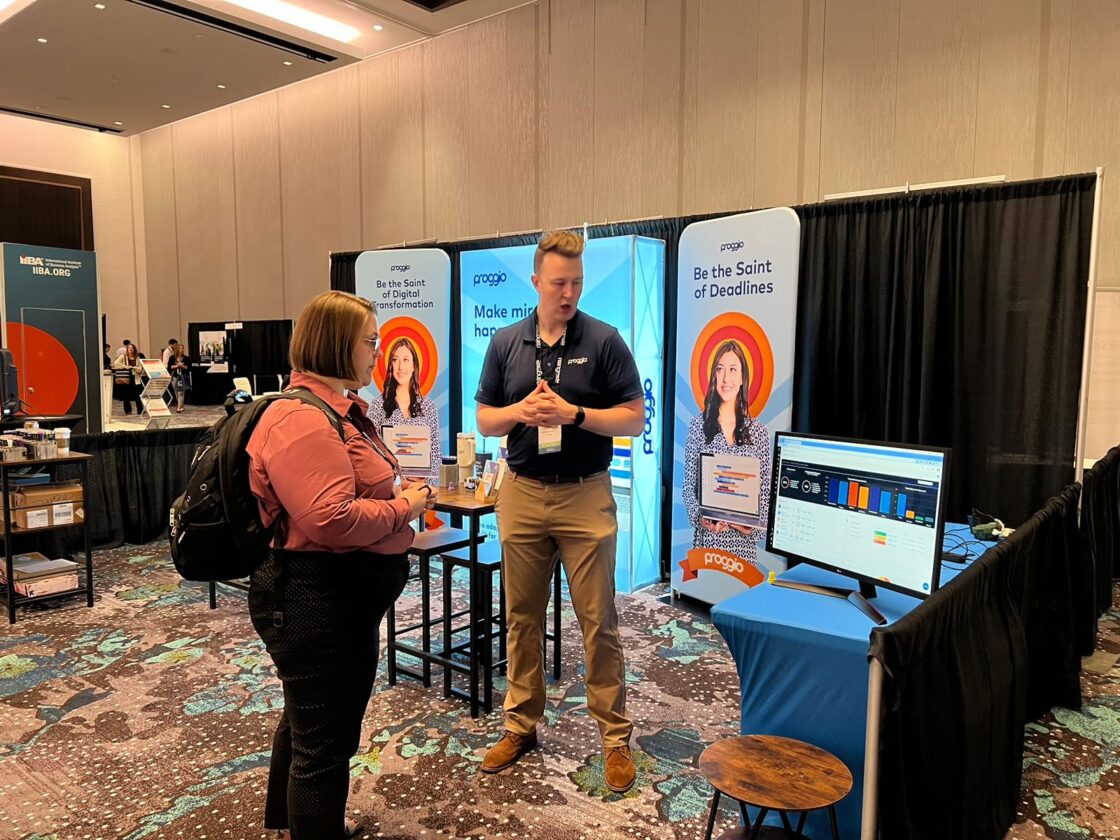 Two people talking at a trade show booth with colorful displays and a monitor.