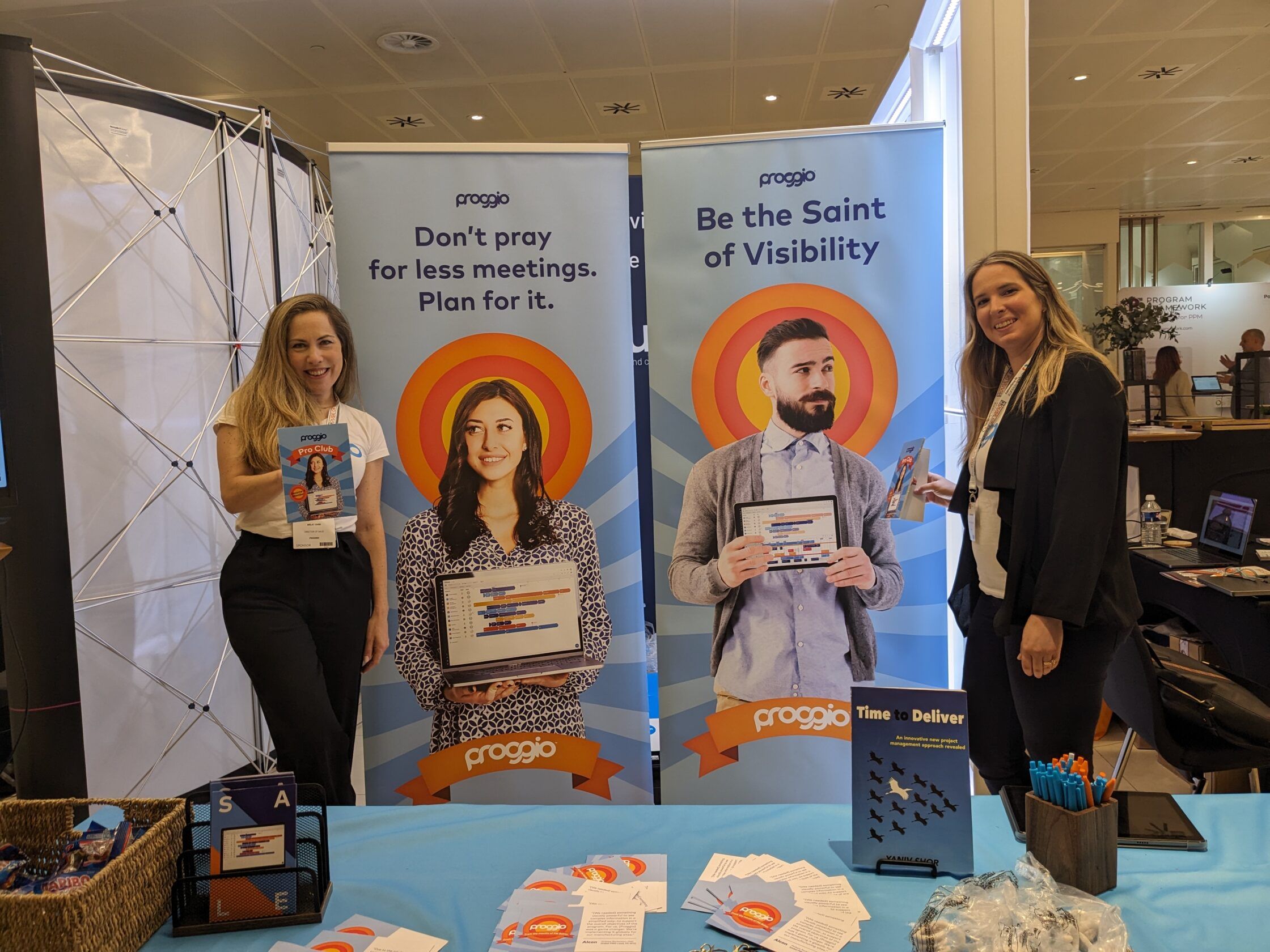 Two women at a trade show booth with promotional banners and materials.