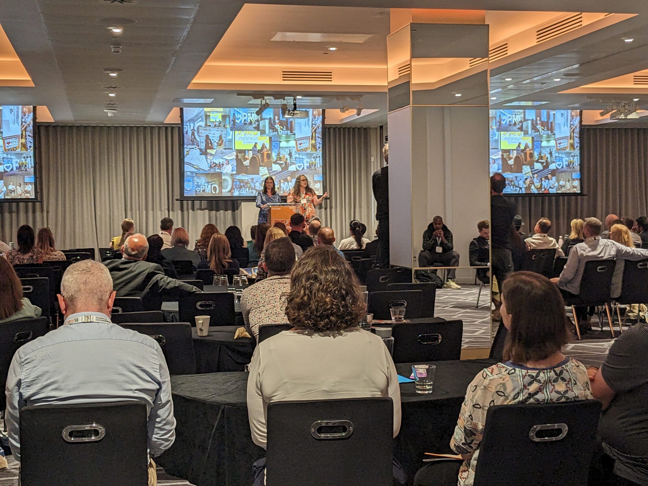 Audience at a conference, focusing on a presentation with slides on a large screen.