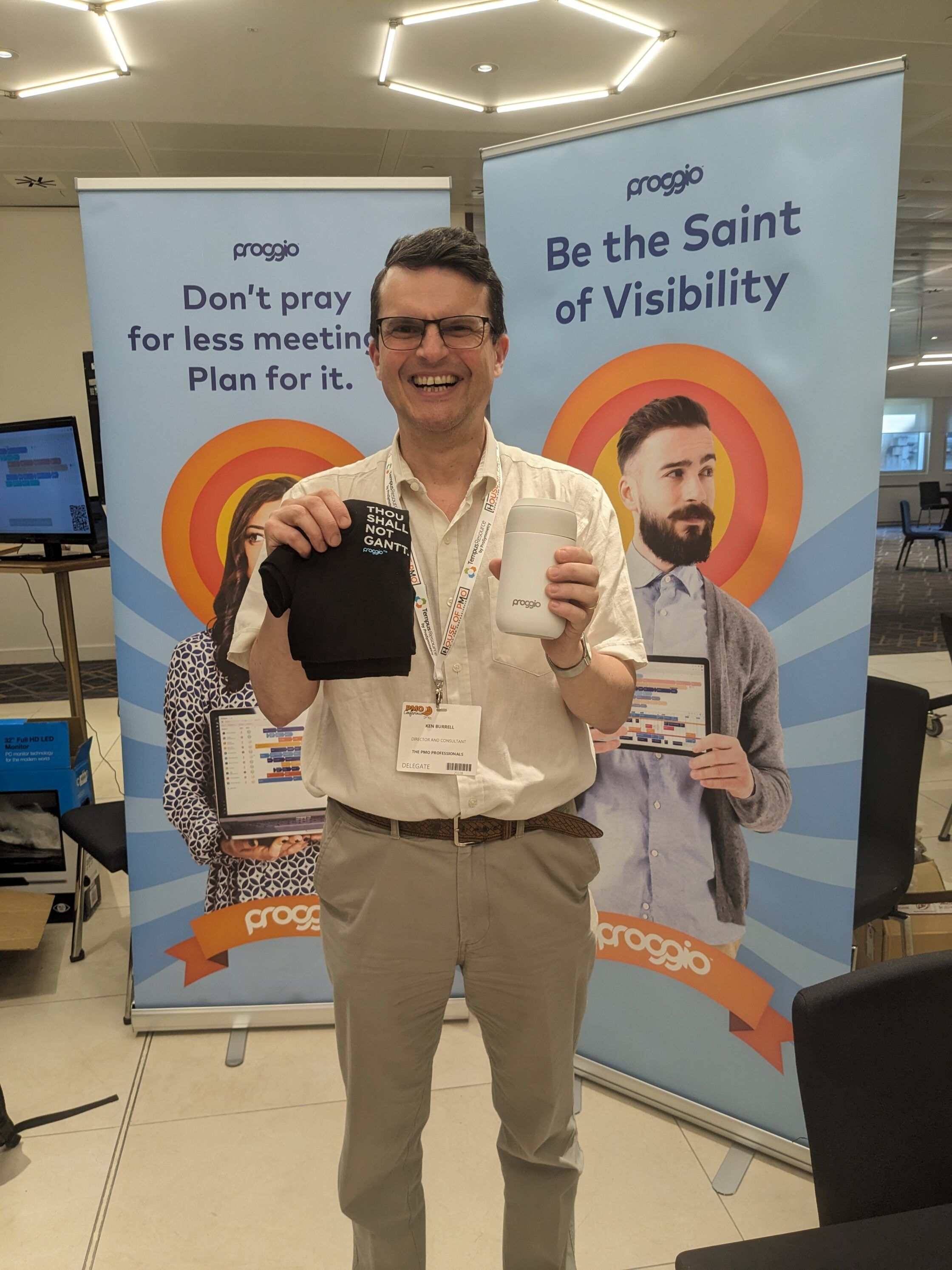 Man smiling and holding products in front of promotional banners at a corporate event.