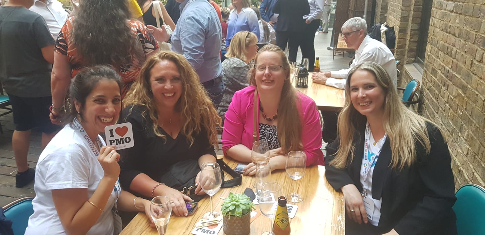 Four women smiling at a table during a social gathering.