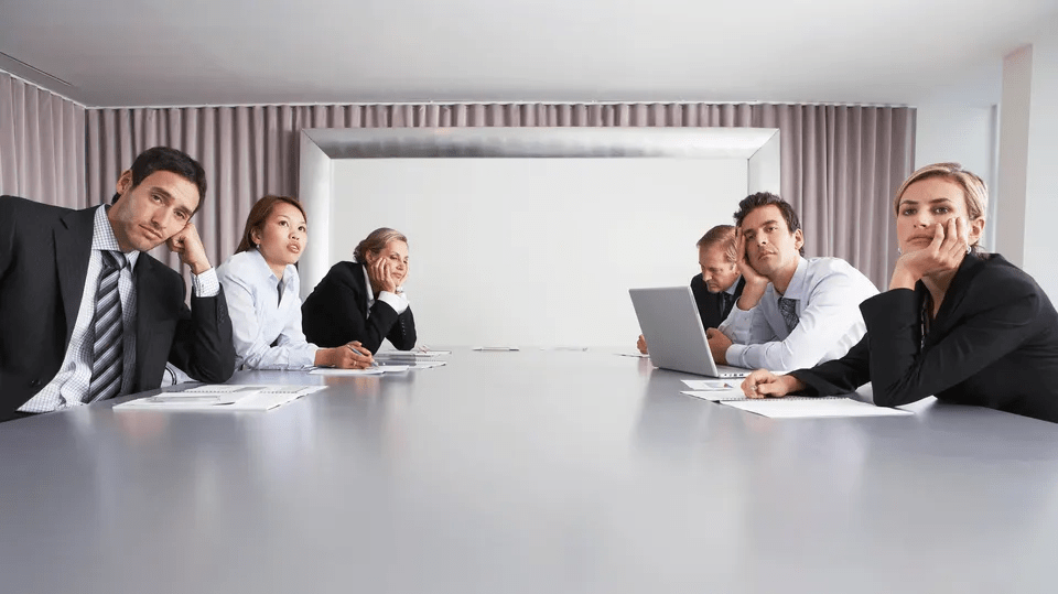 People in formal attire looking bored around a conference table.