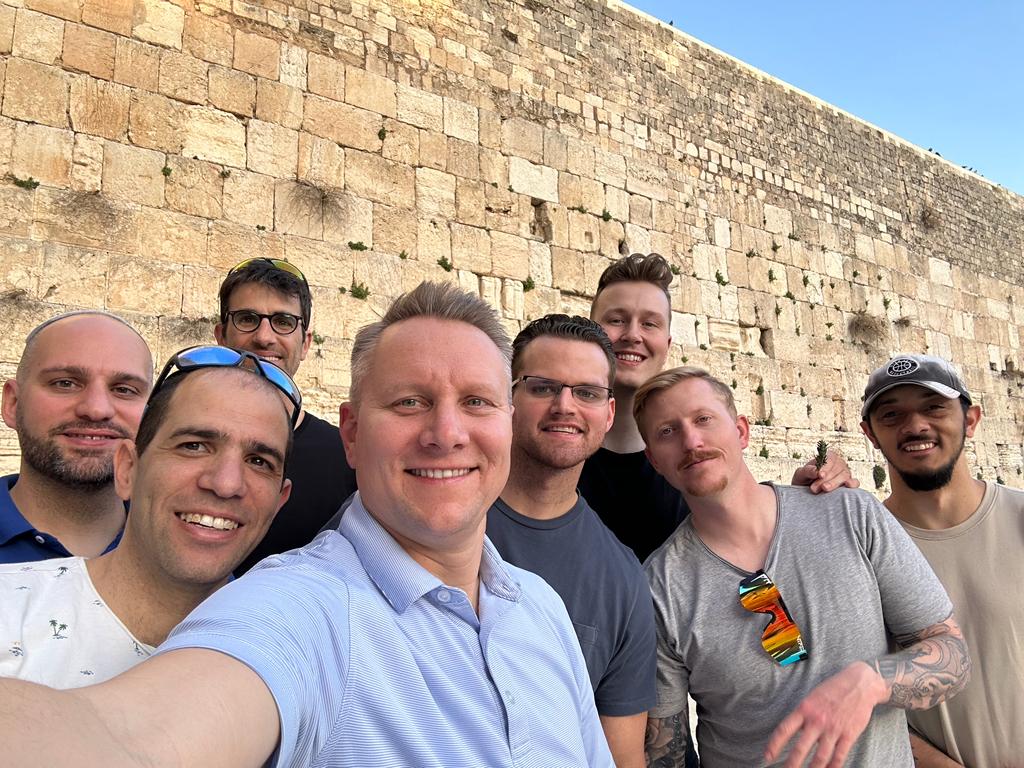 Group of men taking a selfie in front of a large stone wall.