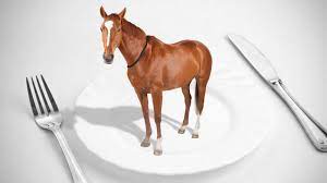 A small horse standing on a white plate, with a fork and knife beside it.