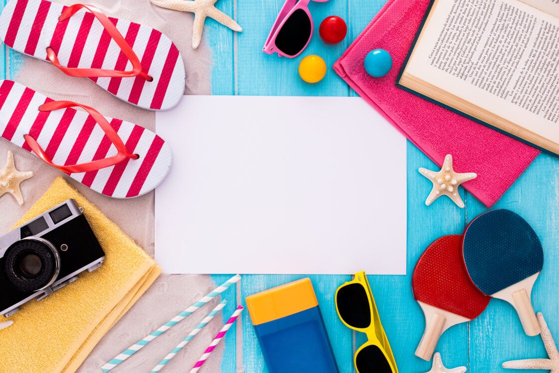 Beach items surround a blank paper on a blue wooden background.