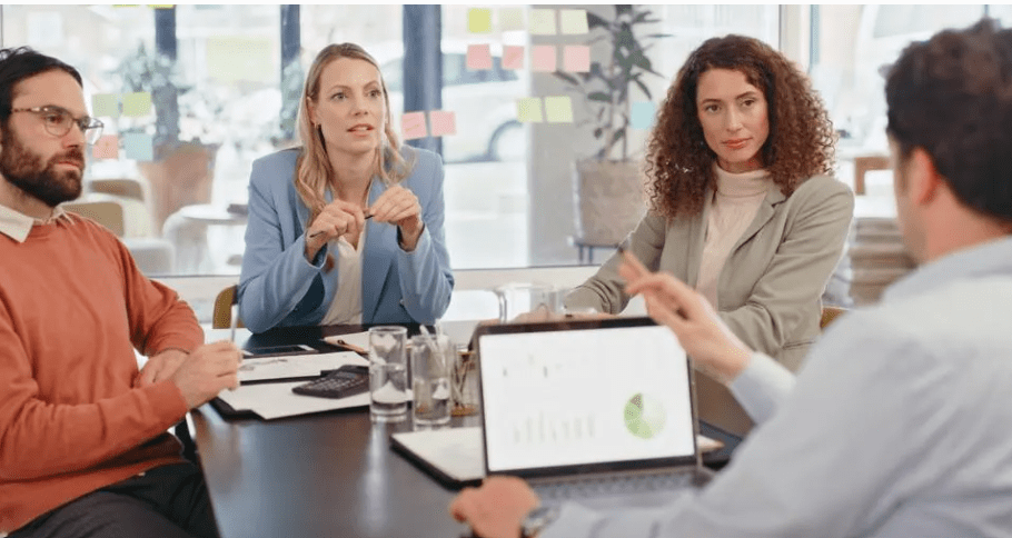 Four people having a business meeting with a laptop and papers on the table.