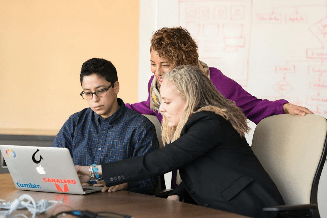 Three people collaborating around a laptop in a meeting room.