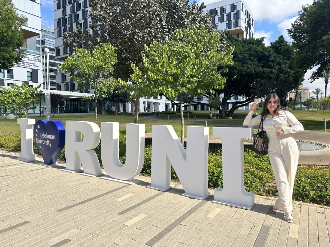 Person posing next to large "I love RUNI" sign at a university campus.