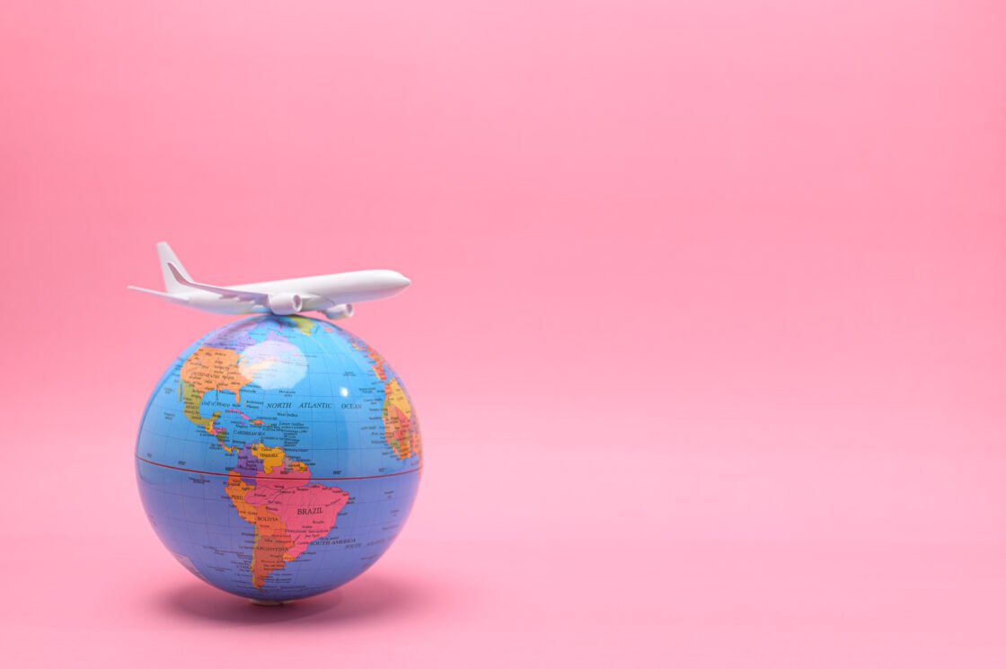 Model airplane on a globe with a pink background.