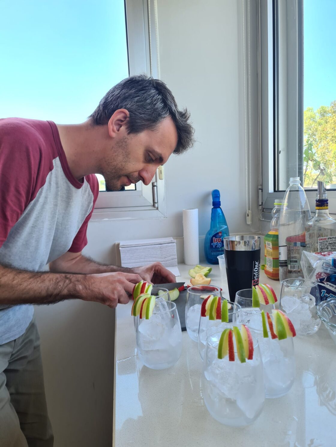 Man cutting apples in a kitchen with prepared drinks on the counter.