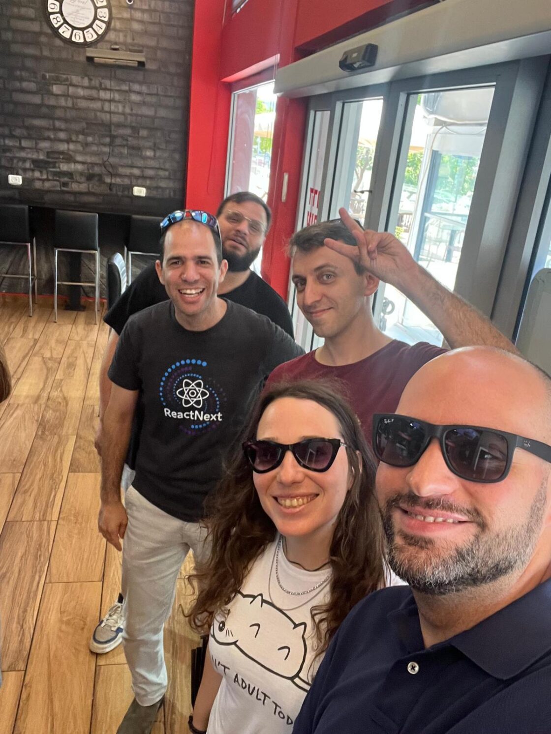 A group of five people smiling and posing in a casual indoor setting.