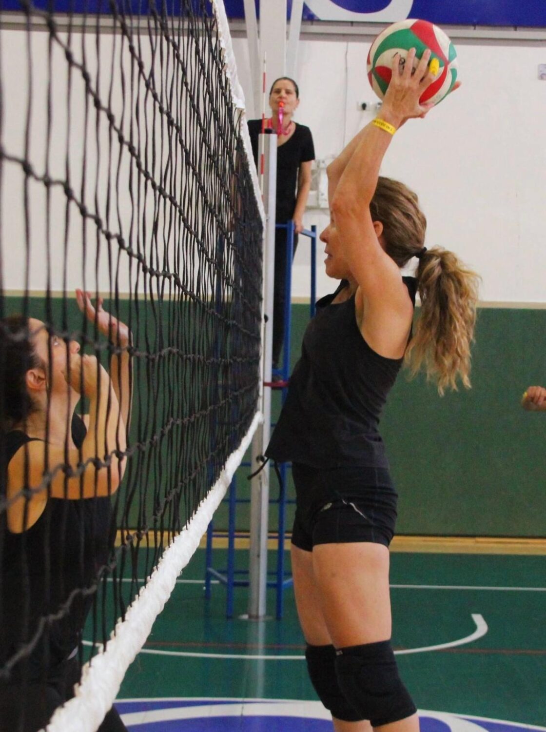 A volleyball player prepares to spike the ball over the net while an opponent blocks.