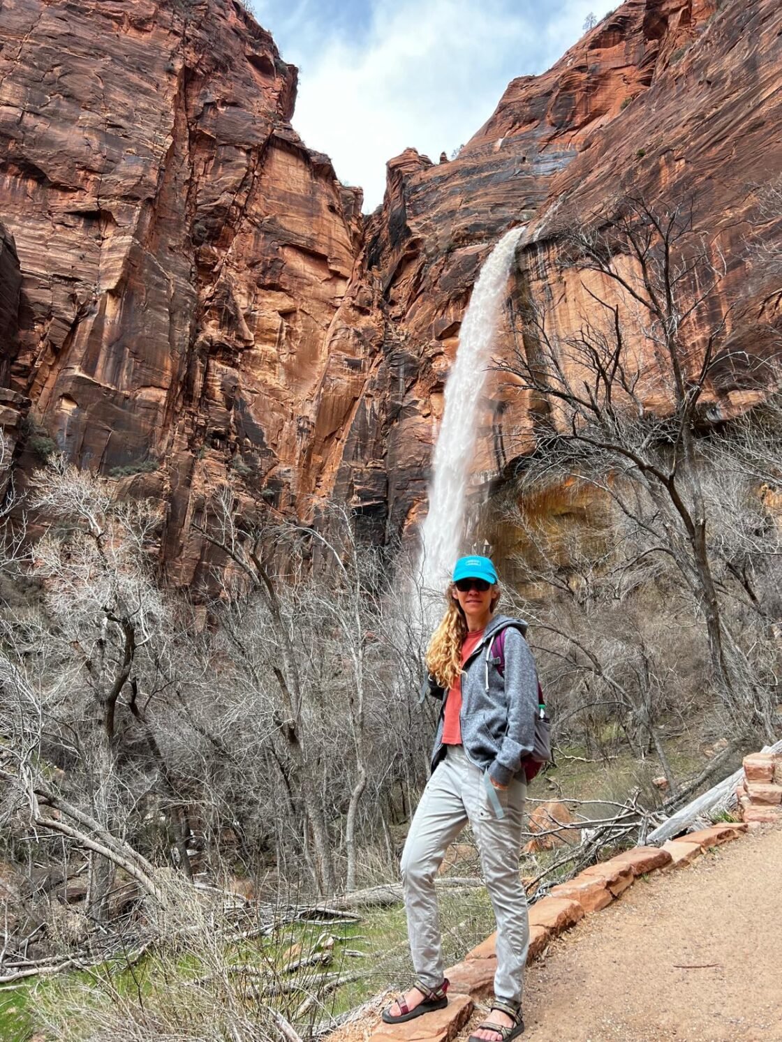 Person posing in front of a waterfall in a rocky canyon landscape.